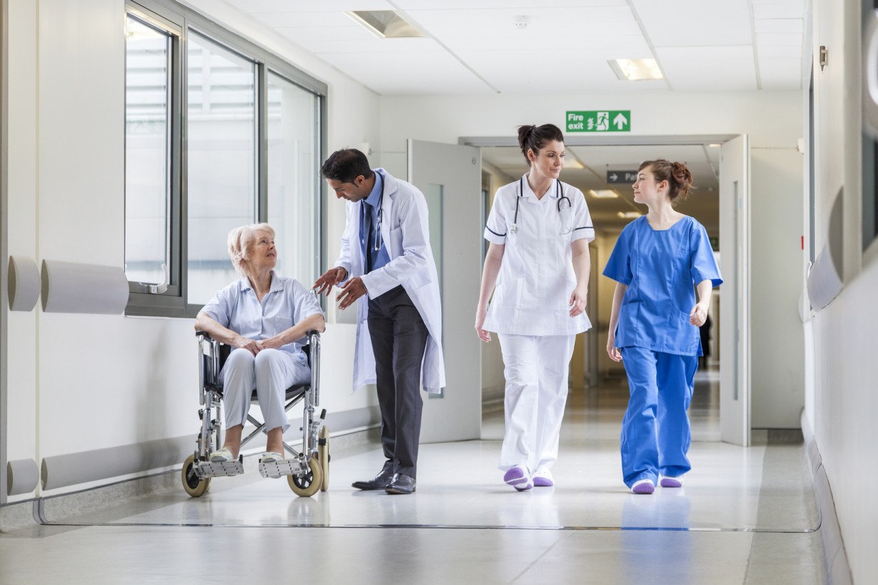 Doctors & nurse in hospital corridor with senior female patient in wheel chair with male Asian doctor