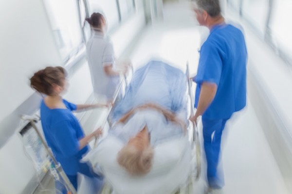 A motion blurred photograph of a senior female patient on stretcher or gurney being pushed at speed through a hospital corridor by doctors & nurses to an emergency room
