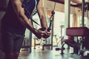 Unrecognizable muscular man in sportswear wrapped up in doing exercise while having workout at spacious gym